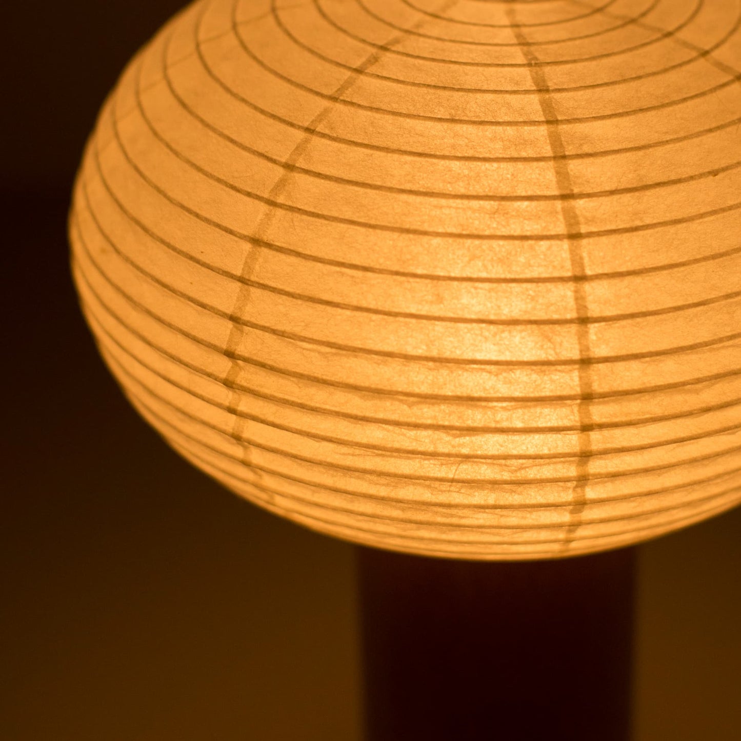 "Nahaufnahme der tragbaren Papierlampe „TORCHIN OVAL“, die die filigrane Handwerkskunst des Lampenschirms aus Washi-Papier und das warme Licht, das sie ausstrahlt, hervorhebt."