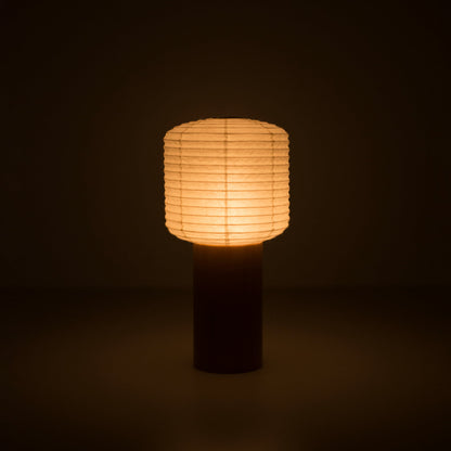 Eine tragbare japanische Papierlampe mit Holzgriff und quadratisch-zylindrischem Papierkopf, die in einem dunklen Raum warmes Licht ausstrahlt