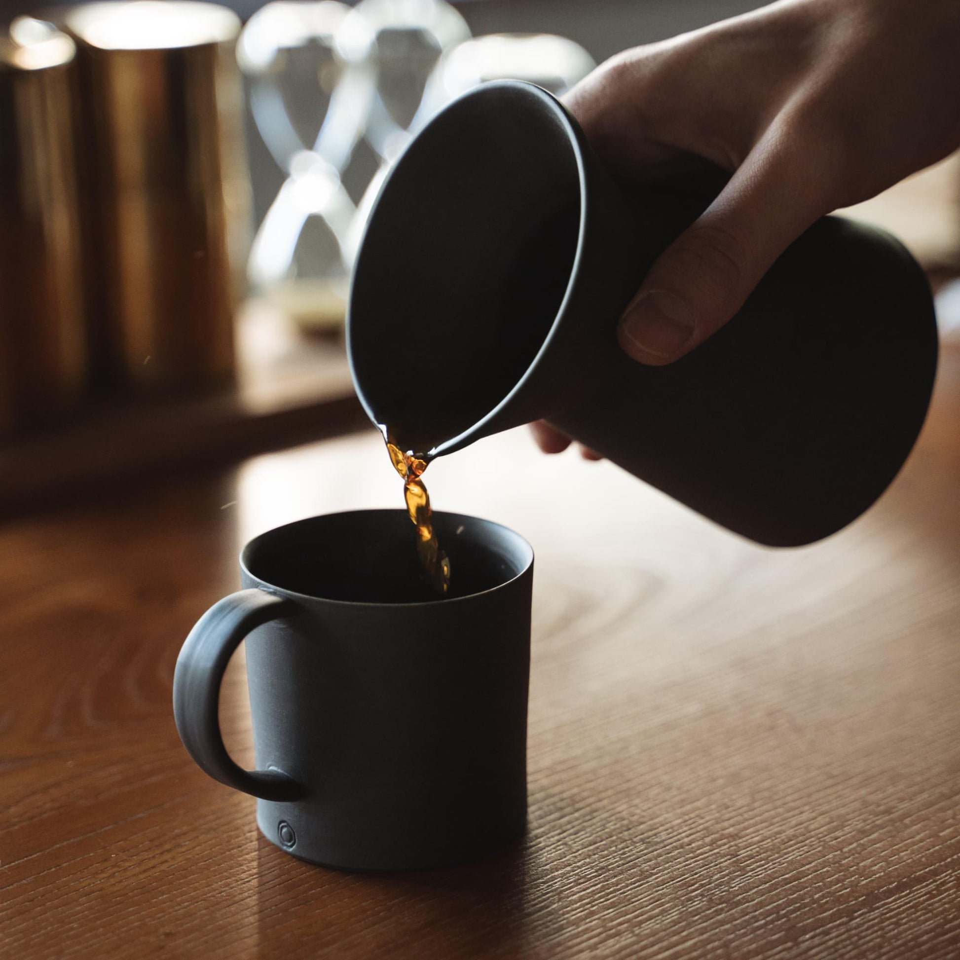 Hælder kaffe fra en minimalistisk sort Banko stel kaffekande op i en sort kop.