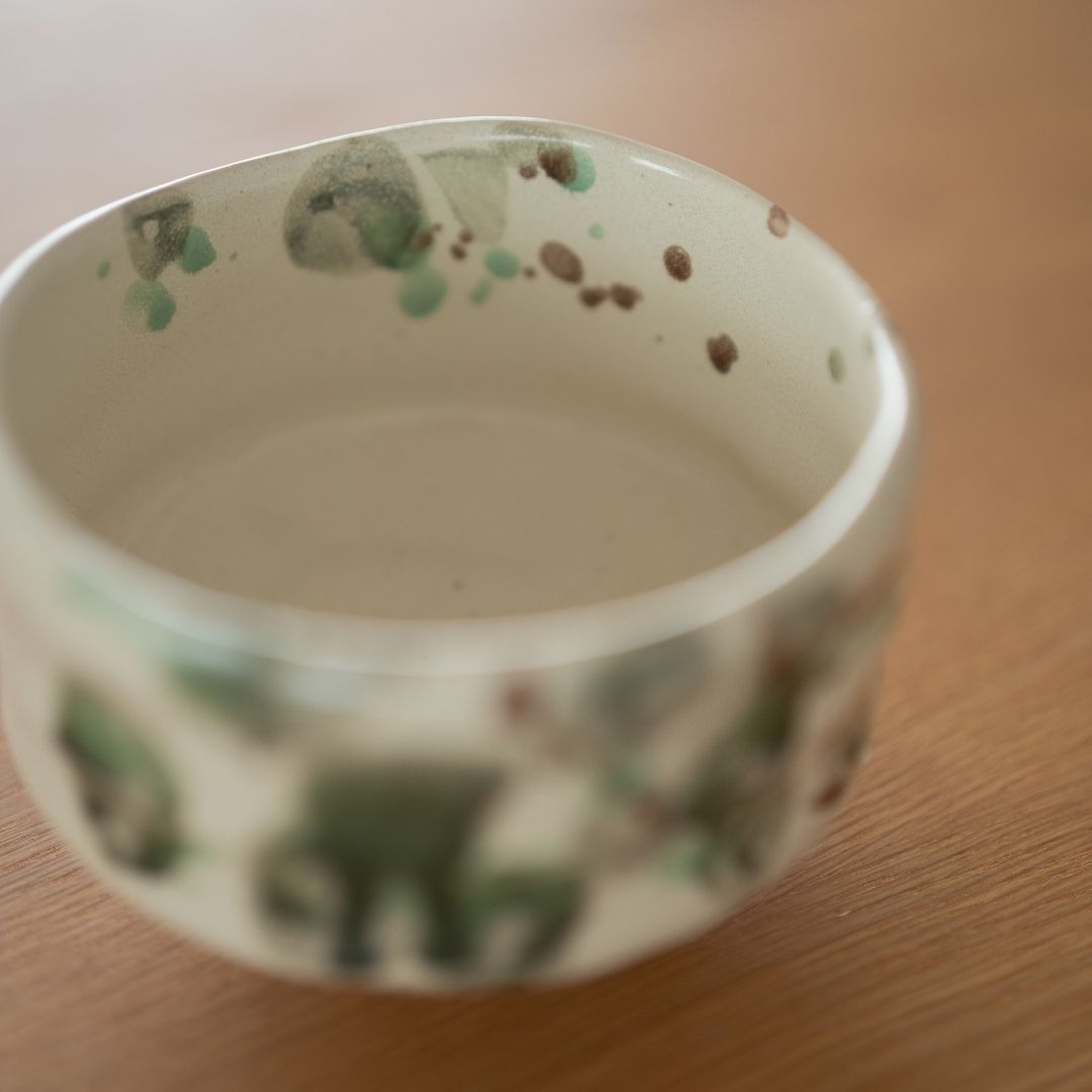 Højt vinkelbillede ind i "Skov" matcha-skålen, der viser den cremede hvide bund, der er plettet med grøn håndværksglasur, hvilket skaber en fredfyldt te-ceremonioplevelse.