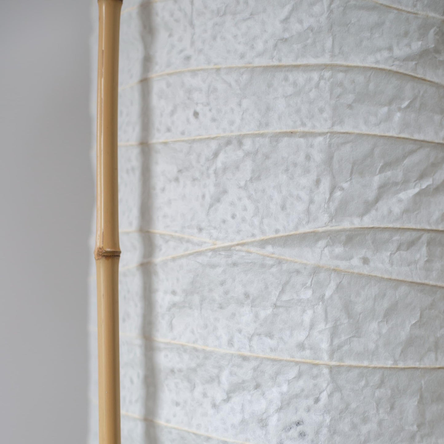 "Vue latérale détaillée d'une lampe japonaise cylindrique, montrant le contraste entre le papier washi blanc doux et le cadre en bambou marron"