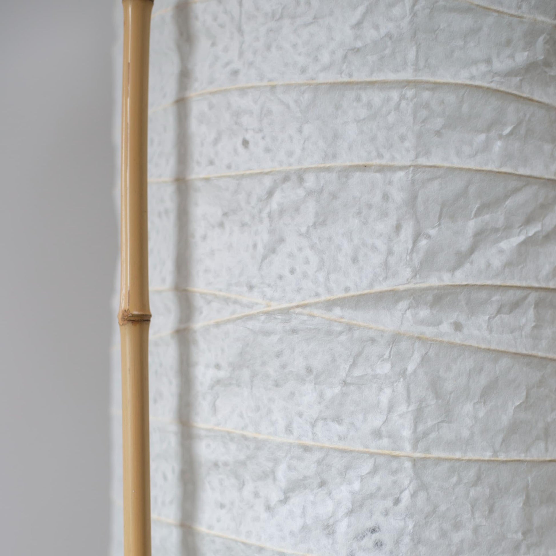 "Vue latérale détaillée d'une lampe japonaise cylindrique, montrant le contraste entre le papier washi blanc doux et le cadre en bambou marron"