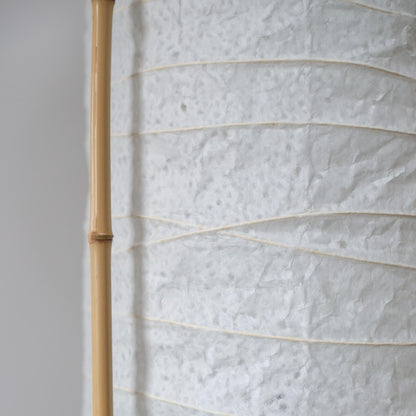 "Vue latérale détaillée d'une lampe japonaise cylindrique, montrant le contraste entre le papier washi blanc doux et le cadre en bambou marron"