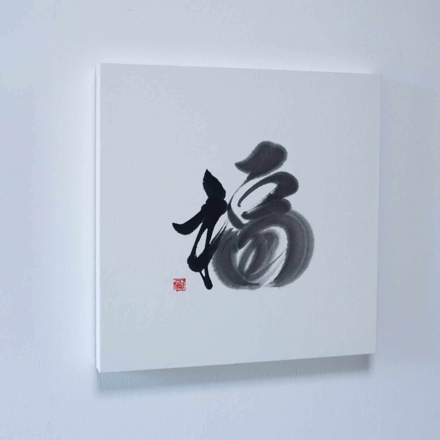 A square wall art panel featuring the calligraphy of '福' (fortune) on white paper, mounted on a white wall. 