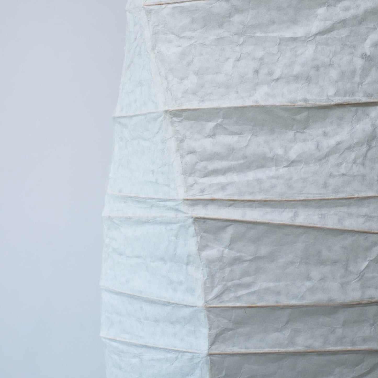 Vue de côté d'une lampe japonaise en papier washi aux courbes fluides, mettant en valeur la beauté et la texture du papier sur fond blanc
