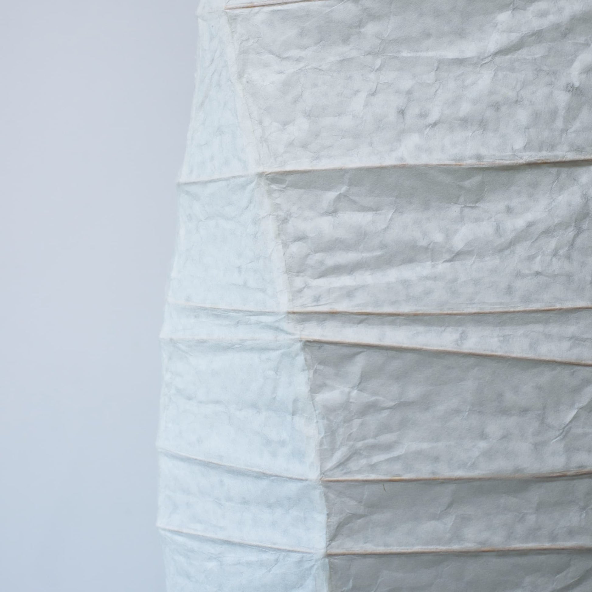 Vue de côté d'une lampe japonaise en papier washi aux courbes fluides, mettant en valeur la beauté et la texture du papier sur fond blanc