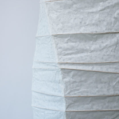 Vue de côté d'une lampe japonaise en papier washi aux courbes fluides, mettant en valeur la beauté et la texture du papier sur fond blanc