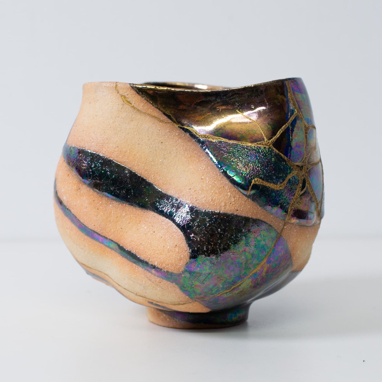 Vue de côté d'un bol à matcha en céramique kintsugi avec des coutures dorées et une forme naturelle wabi-sabi