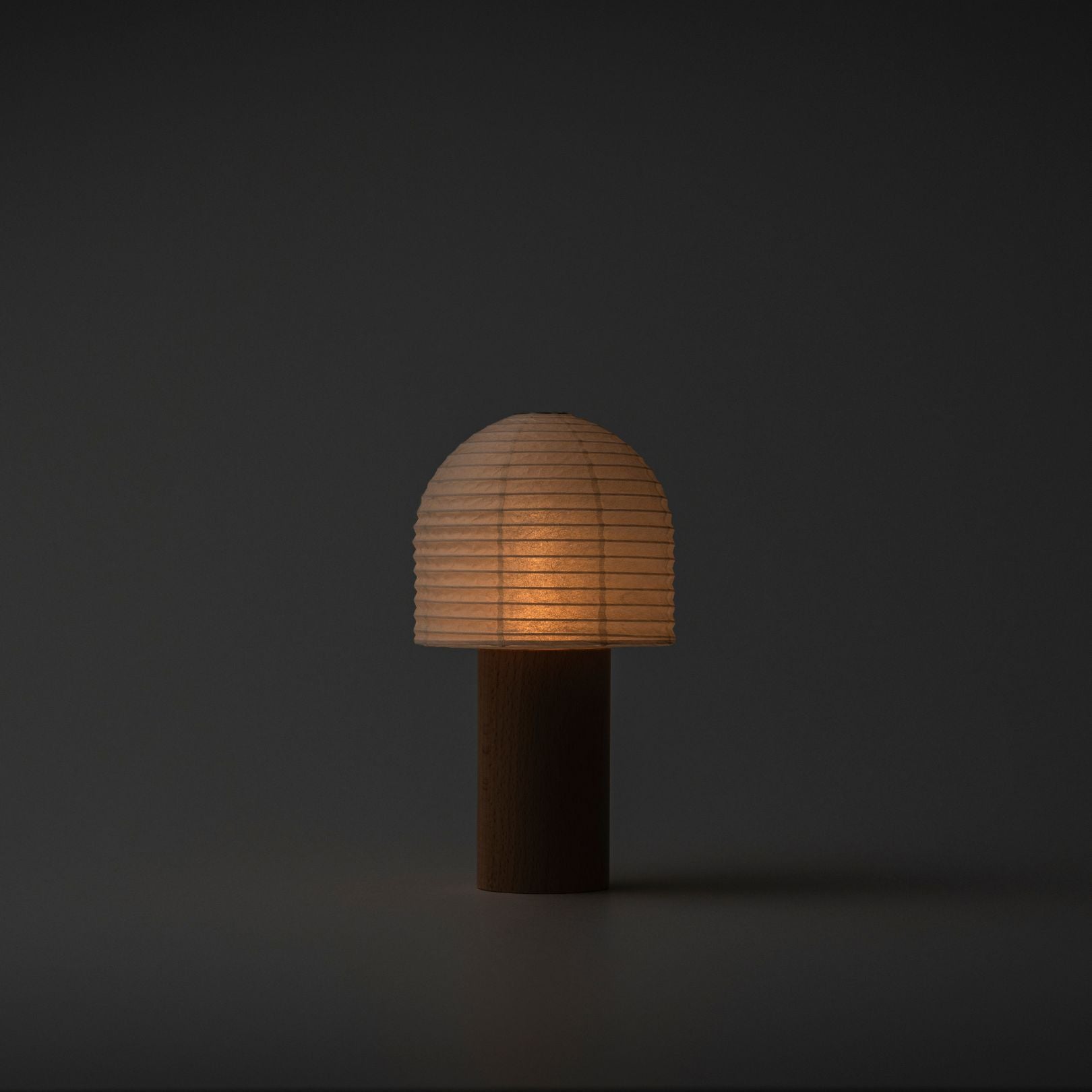 A softly glowing Japanese paper lantern with a bell-shaped top and wooden handle in a dark room