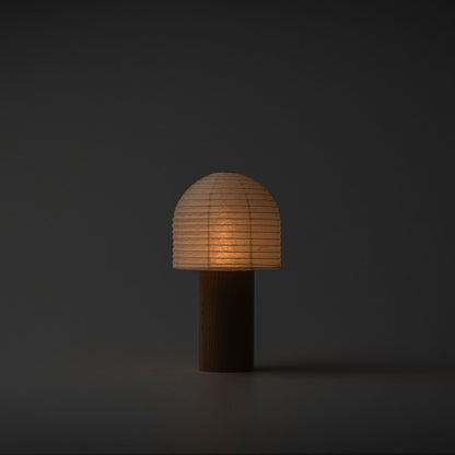 A softly glowing Japanese paper lantern with a bell-shaped top and wooden handle in a dark room