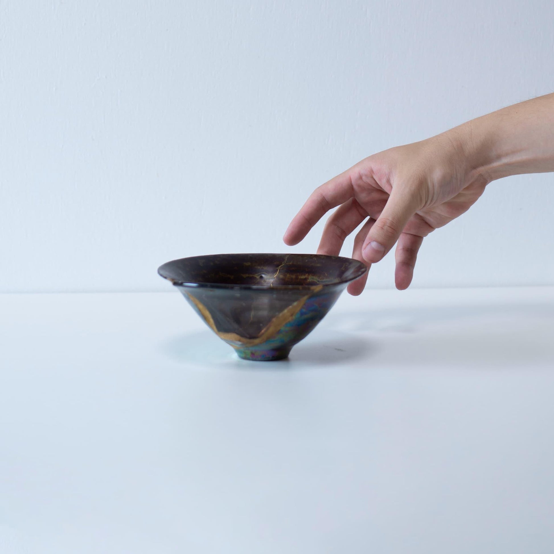 Eine Hand, die eine Kintsugi-reparierte Schale hält und die filigranen Goldlinien zeigt, die das zerbrochene Stück ausbessern.