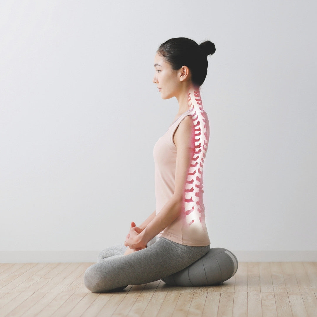 Ryggen på en kvinde, mens hun sidder i lotusstilling og mediterer med en japansk meditationspude Zafu