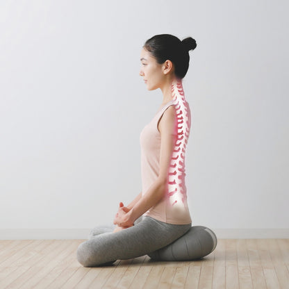 Ryggen på en kvinde, mens hun sidder i lotusstilling og mediterer med en japansk meditationspude Zafu