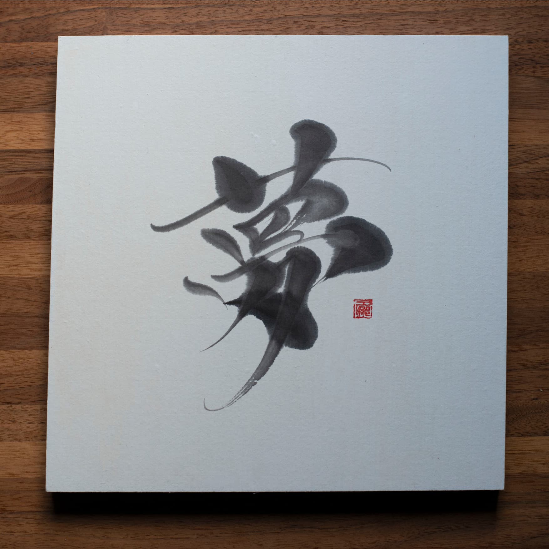 Een foto van bovenaf van een vierkant paneel met het Japanse karakter voor "droom" (夢) geschreven in kalligrafie, geplaatst op een houten tafel.