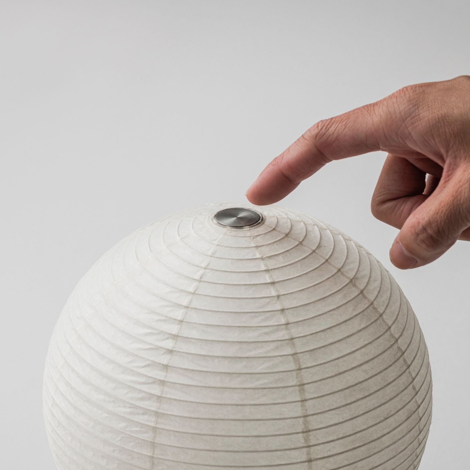 Eine Touch-Lampenschirm-Lampe mit einem Helligkeitsregler am Lampenschirm oben, wobei eine Hand den Schalter betätigt