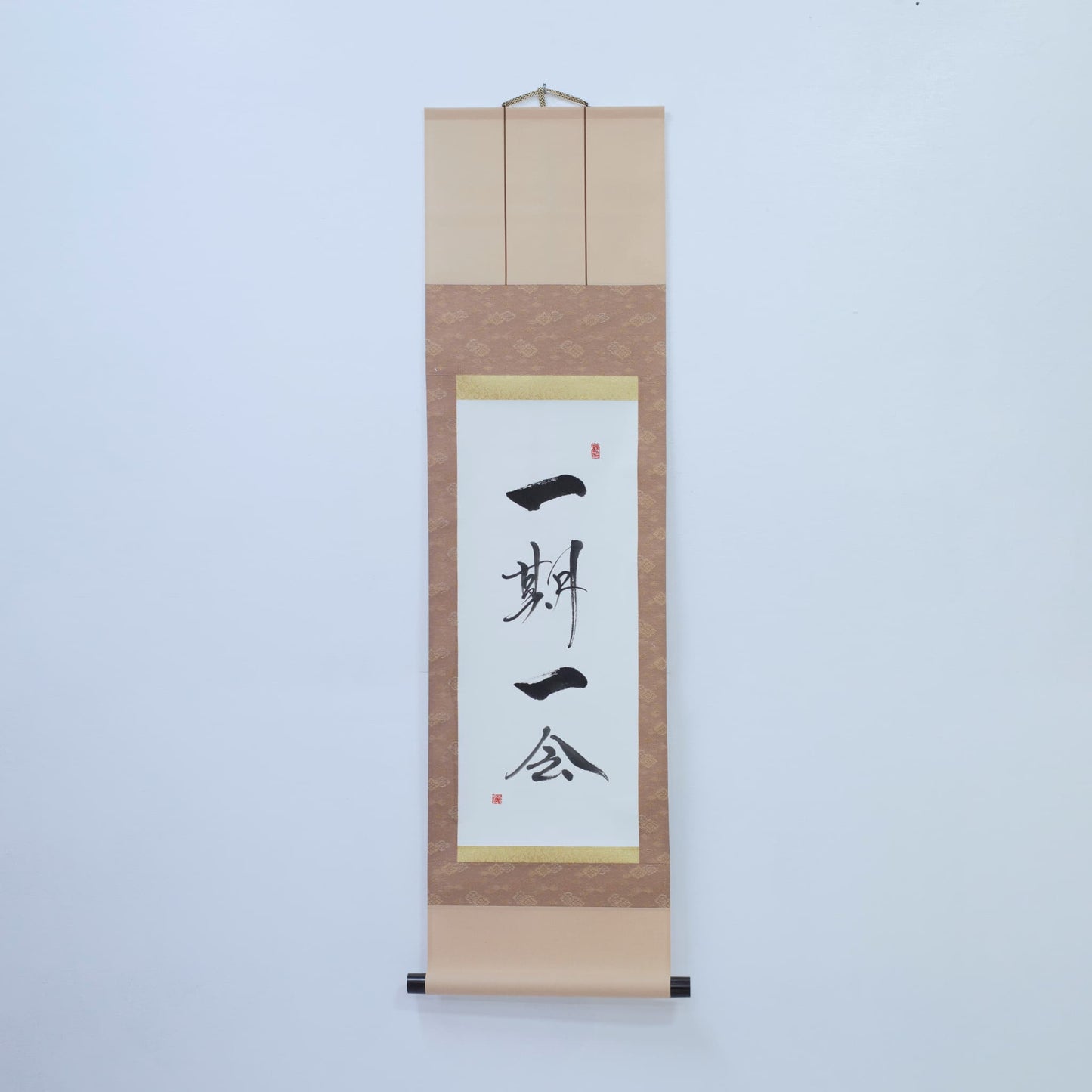 Braune Hängeschriftrolle mit japanischer Kalligrafie von '一期一会' (einmalige Begegnung) auf weißem Reispapier, montiert an einer weißen Wand
