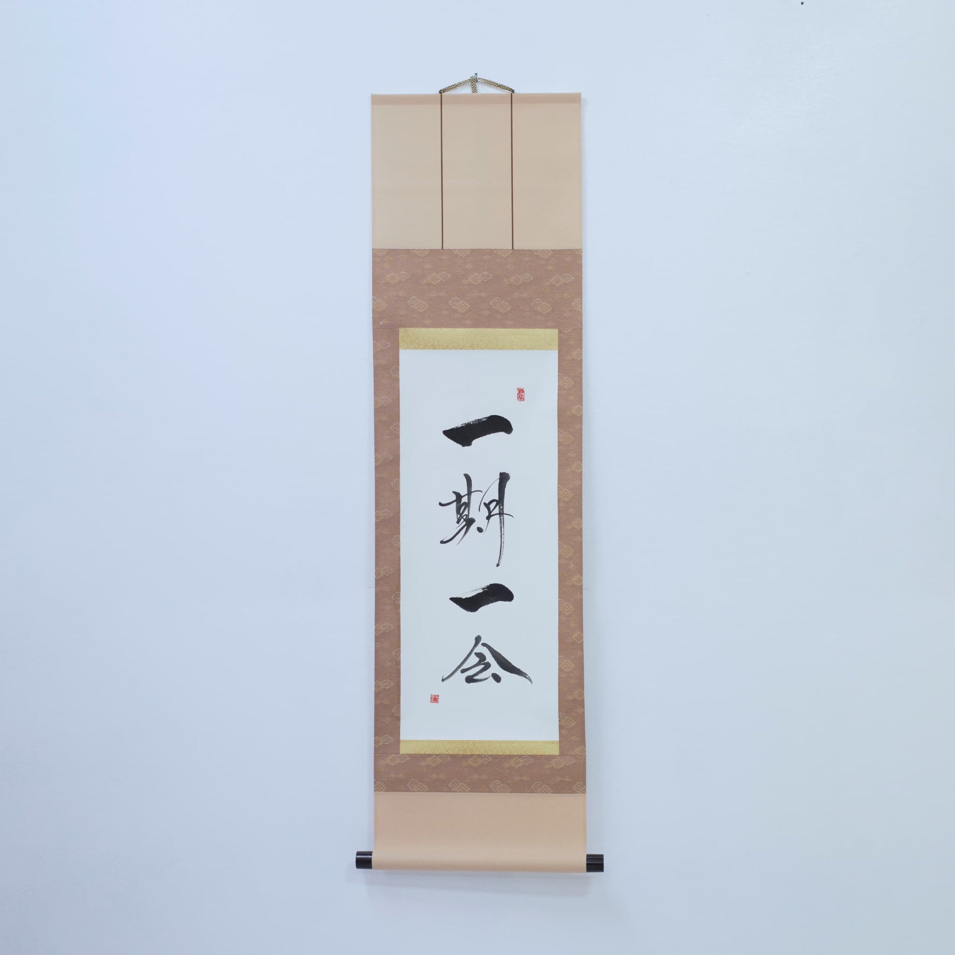 Braune Hängeschriftrolle mit japanischer Kalligrafie von '一期一会' (einmalige Begegnung) auf weißem Reispapier, montiert an einer weißen Wand