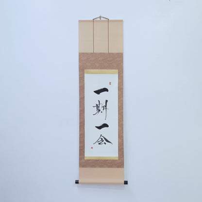Braune Hängeschriftrolle mit japanischer Kalligrafie von '一期一会' (einmalige Begegnung) auf weißem Reispapier, montiert an einer weißen Wand