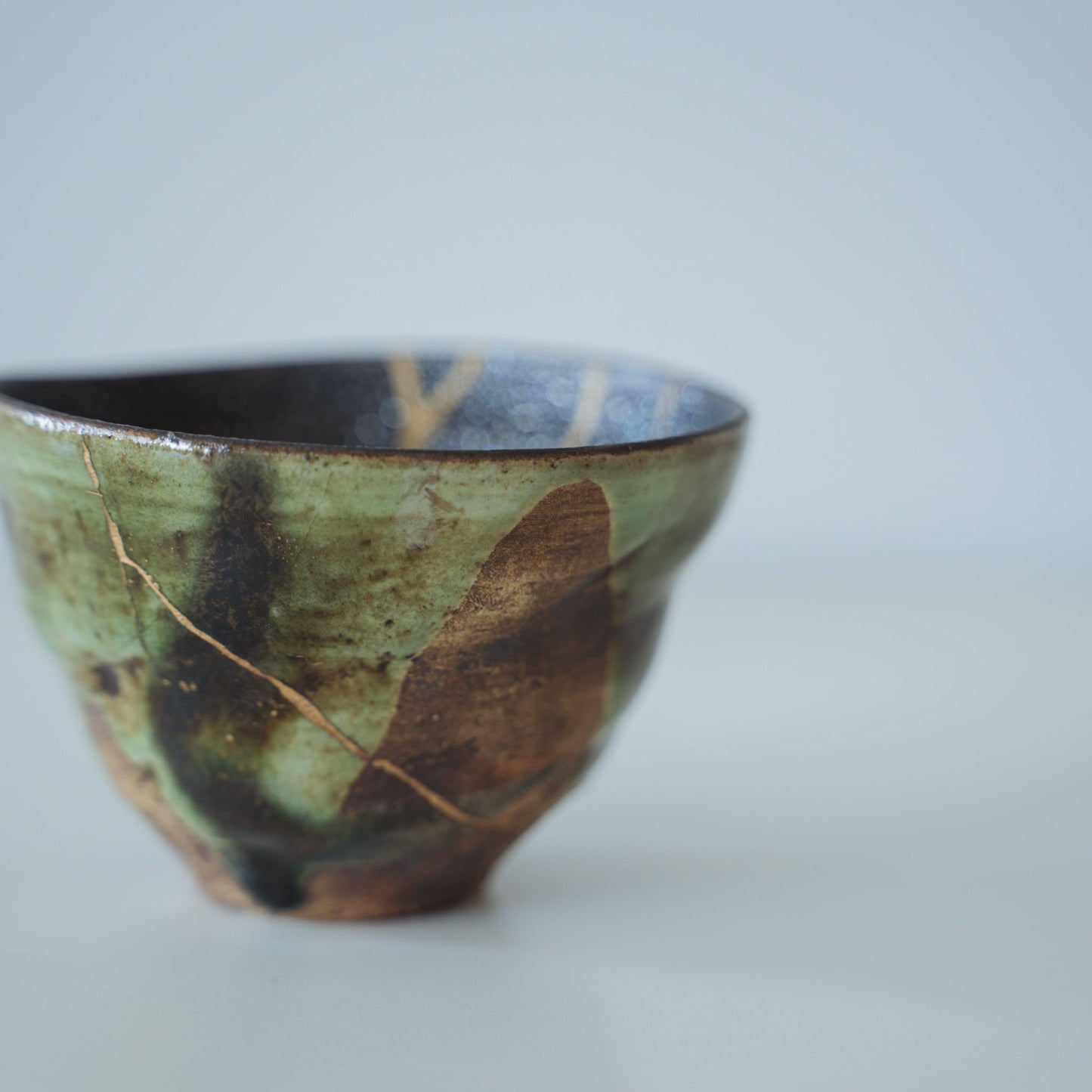 Dybgrøn te-skål repareret med Kintsugi, en traditionel japansk teknik, der viser skønheden i uperfekthed.