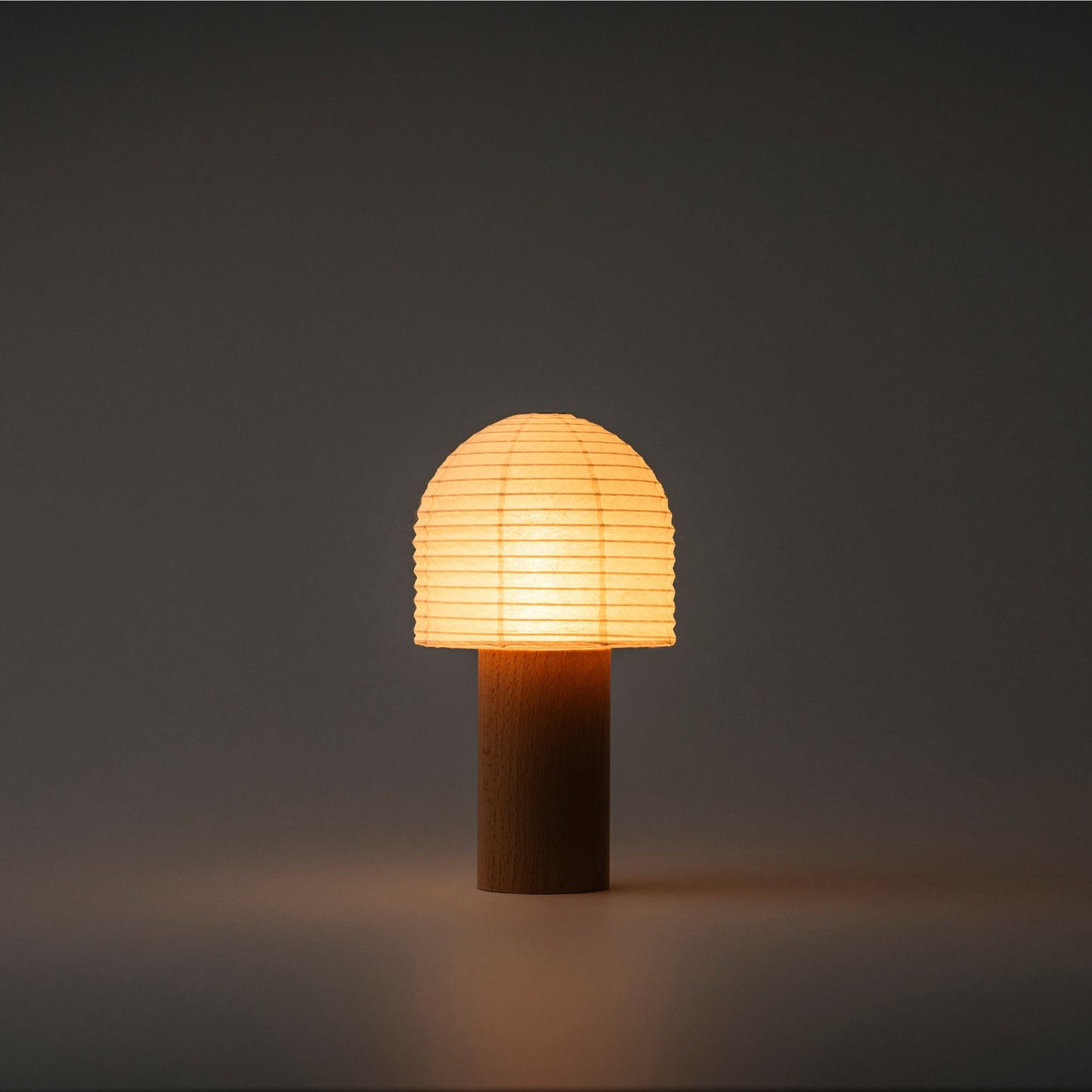 A Japanese paper lantern with a bell-shaped top and wooden handle, emitting bright warm light in a dark room