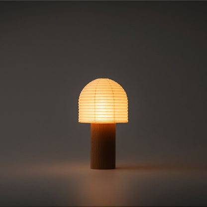 A Japanese paper lantern with a bell-shaped top and wooden handle, emitting bright warm light in a dark room