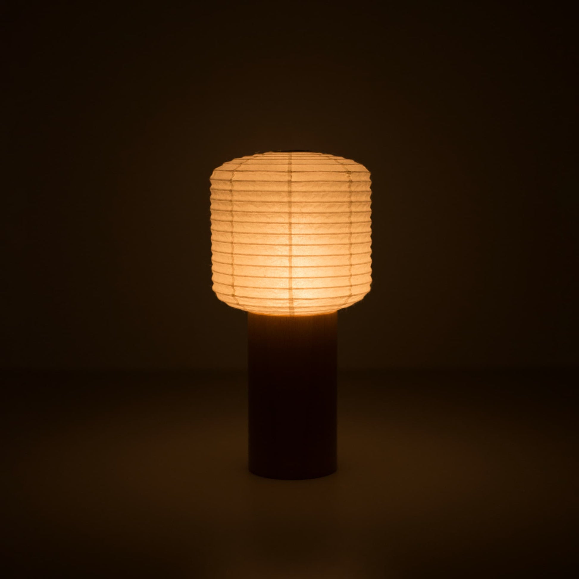 Eine tragbare Papierlampe mit einem kleinen Papierlaternen-Oberteil und Holzgriff, die in einem dunklen Raum warm leuchtet