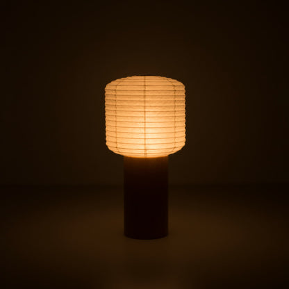 Eine tragbare Papierlampe mit einem kleinen Papierlaternen-Oberteil und Holzgriff, die in einem dunklen Raum warm leuchtet