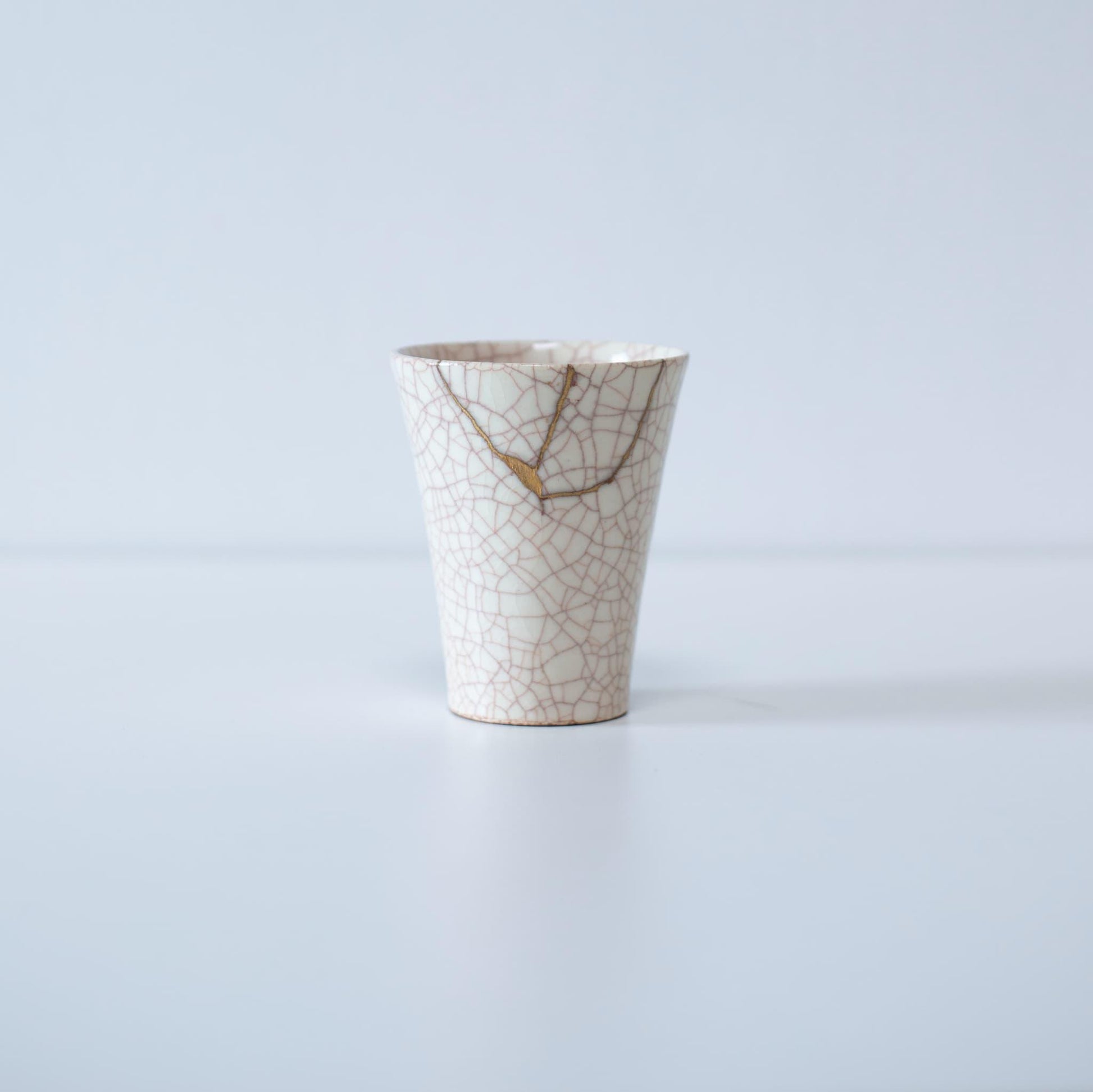 Hvid kop repareret med Kintsugi, en traditionel japansk teknik, præsenteret i en paulownia-trækasse med inskriptionen "Kintsugi".