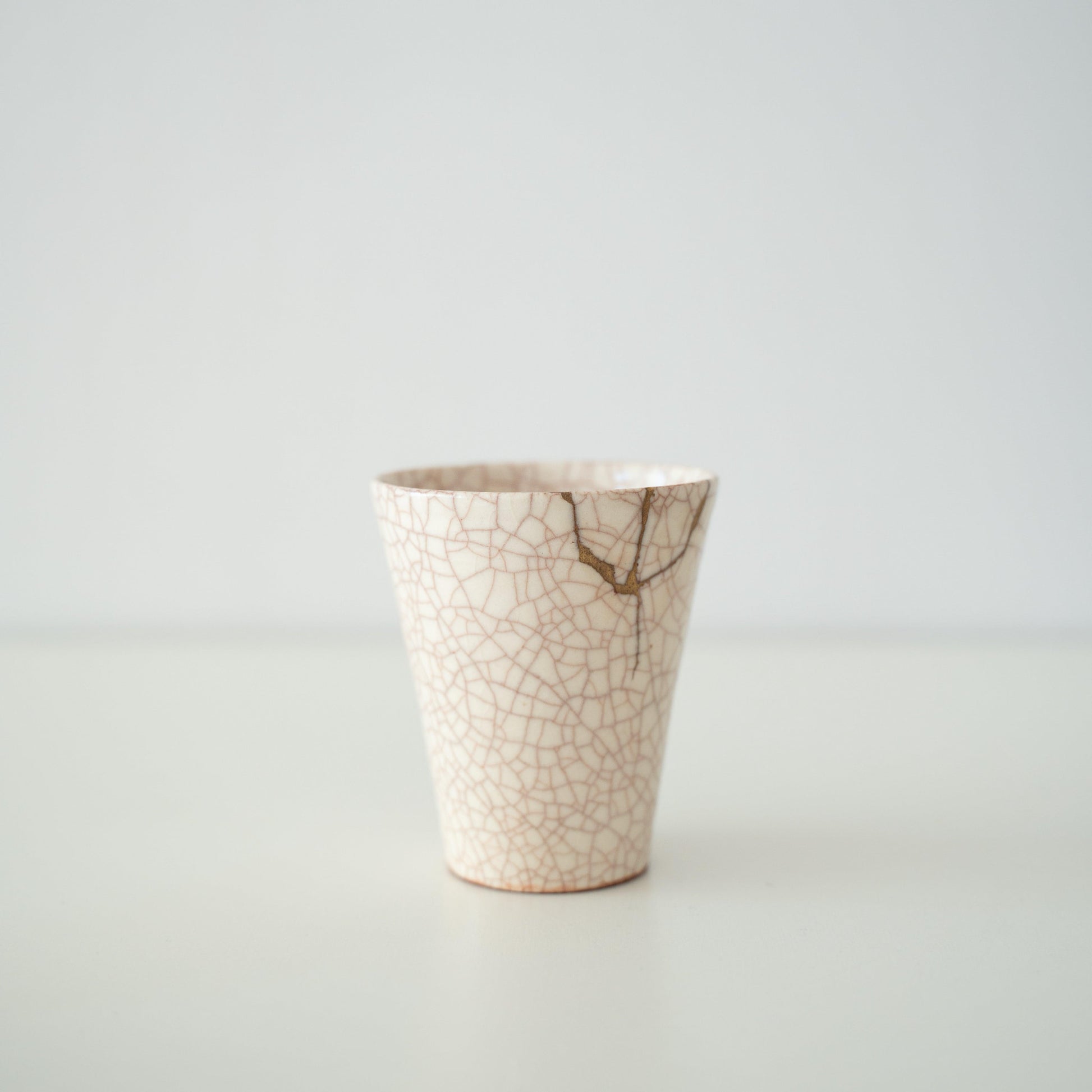 Hvid keramisk kop repareret med kintsugi, en traditionel japansk kunstform til at reparere knust keramik med guldlak, der viser skønheden i uperfekthed og omfavner konceptet wabi-sabi.