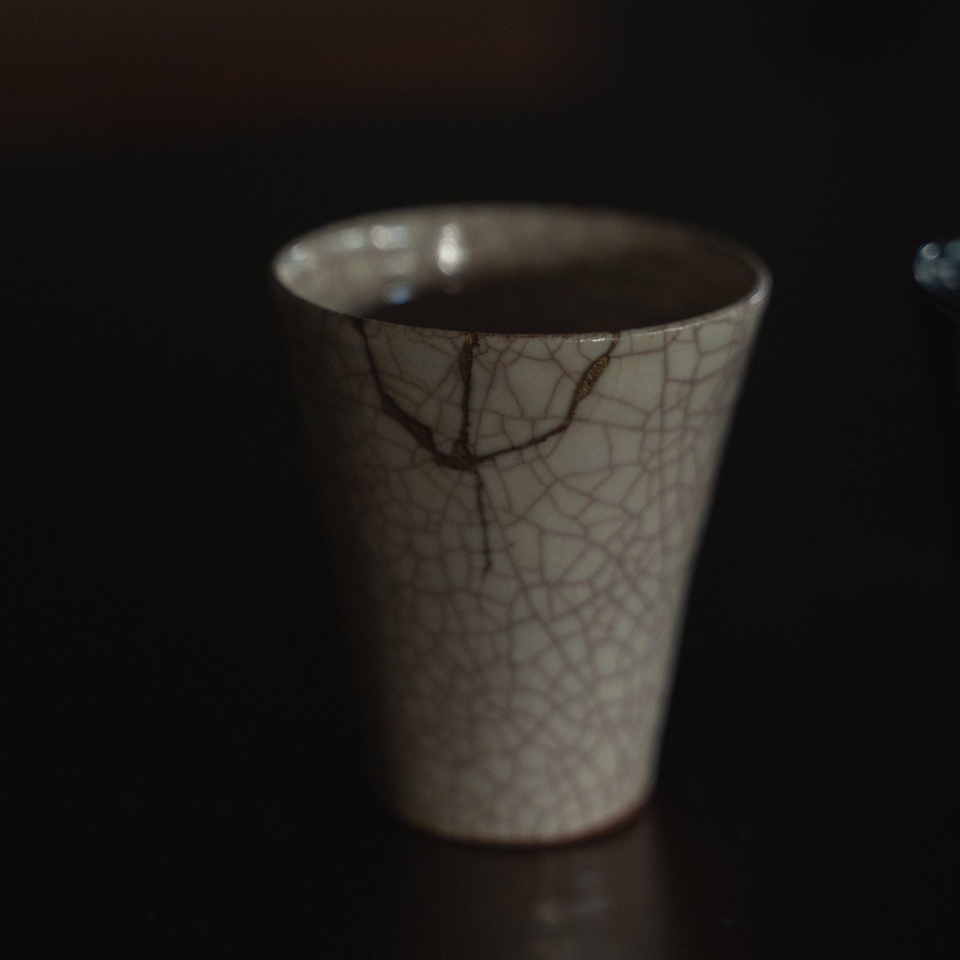 Hvid keramisk kop repareret med kintsugi, en traditionel japansk kunstform til at reparere knust keramik med guldlak, der viser skønheden i uperfekthed og omfavner konceptet wabi-sabi.
