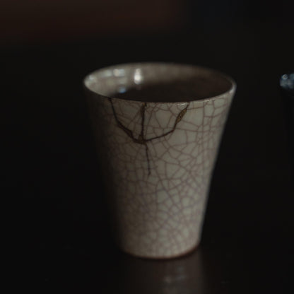 Hvid keramisk kop repareret med kintsugi, en traditionel japansk kunstform til at reparere knust keramik med guldlak, der viser skønheden i uperfekthed og omfavner konceptet wabi-sabi.