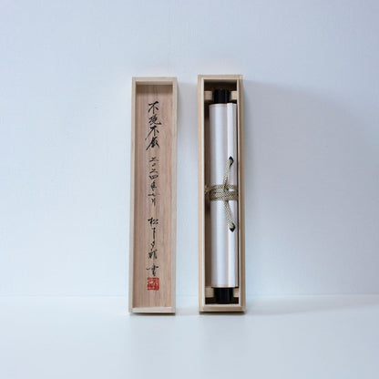Eine lange, schlanke Holzkiste mit Deckel, die zur Aufbewahrung einer traditionellen japanischen Hänge-Schriftrolle dient und die aufgerollte Schriftrolle im Inneren zeigt