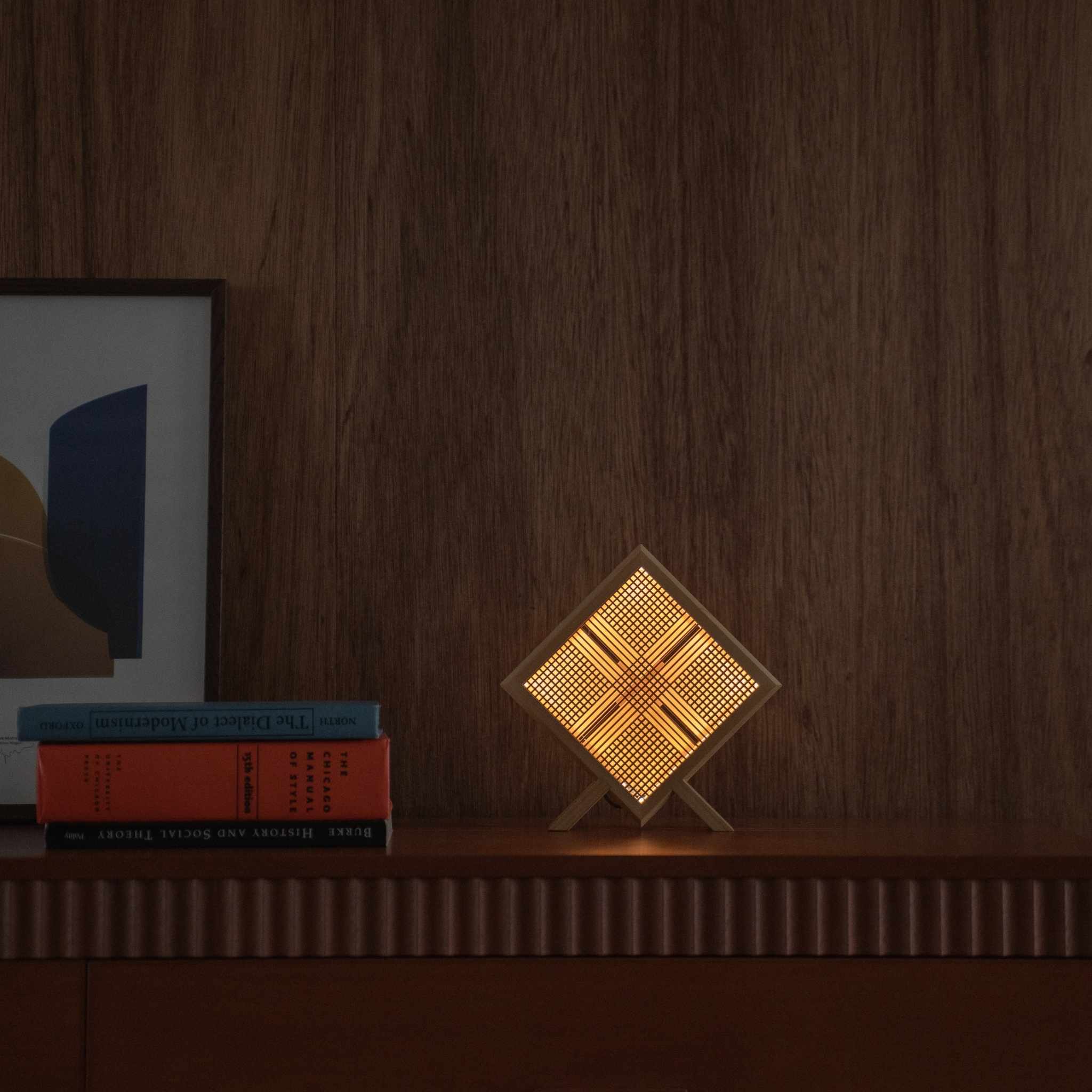 Lit Japanese wood table lamp "Kanata" acting as an ambient lamp, projecting X-shaped art on a mid-century modern console table.