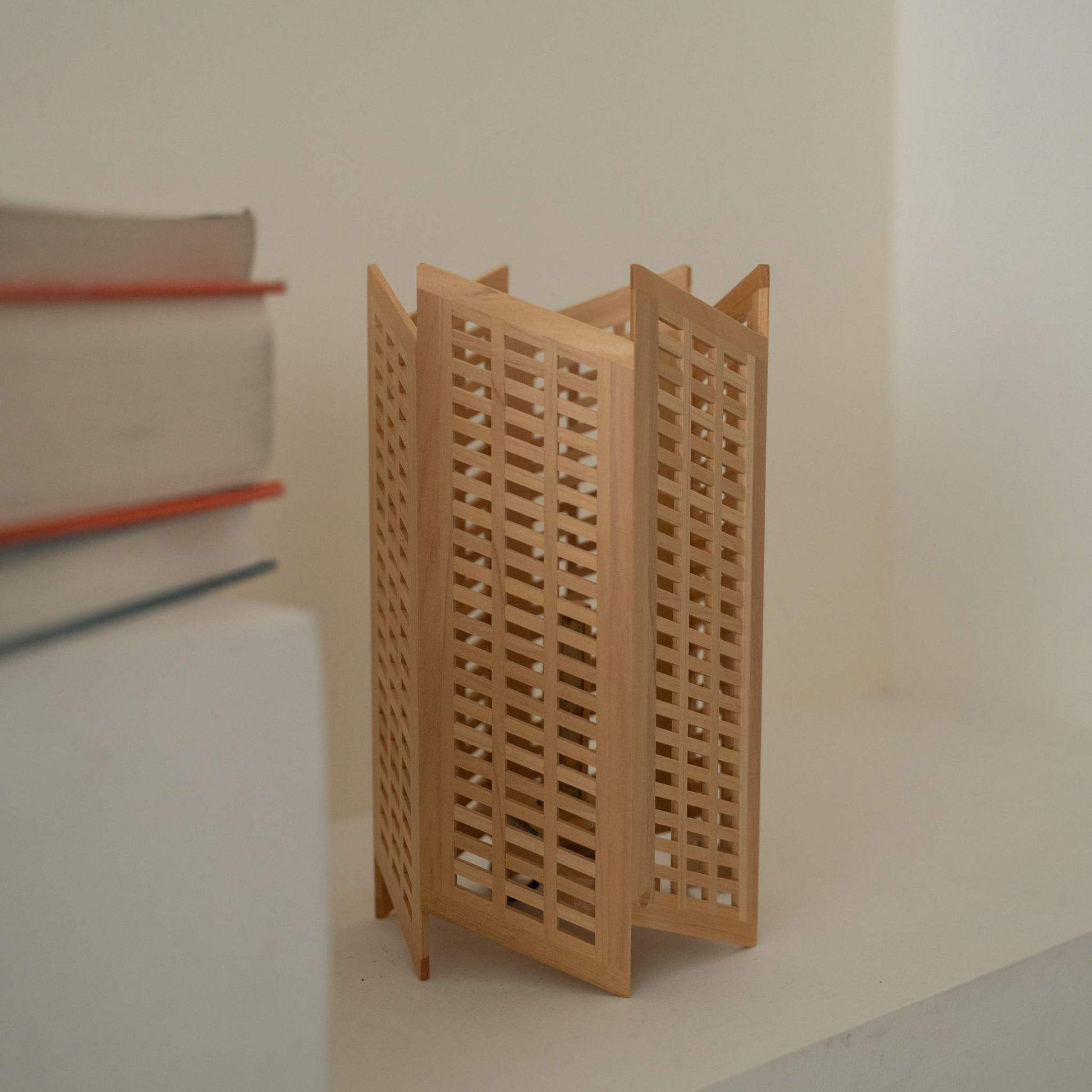 "Nahaufnahme einer japanischen Holz-Tischlampe „Towaru“ neben Büchern, die aufwendige Kumiko-Holzarbeiten an einer Holzlampe zeigt."