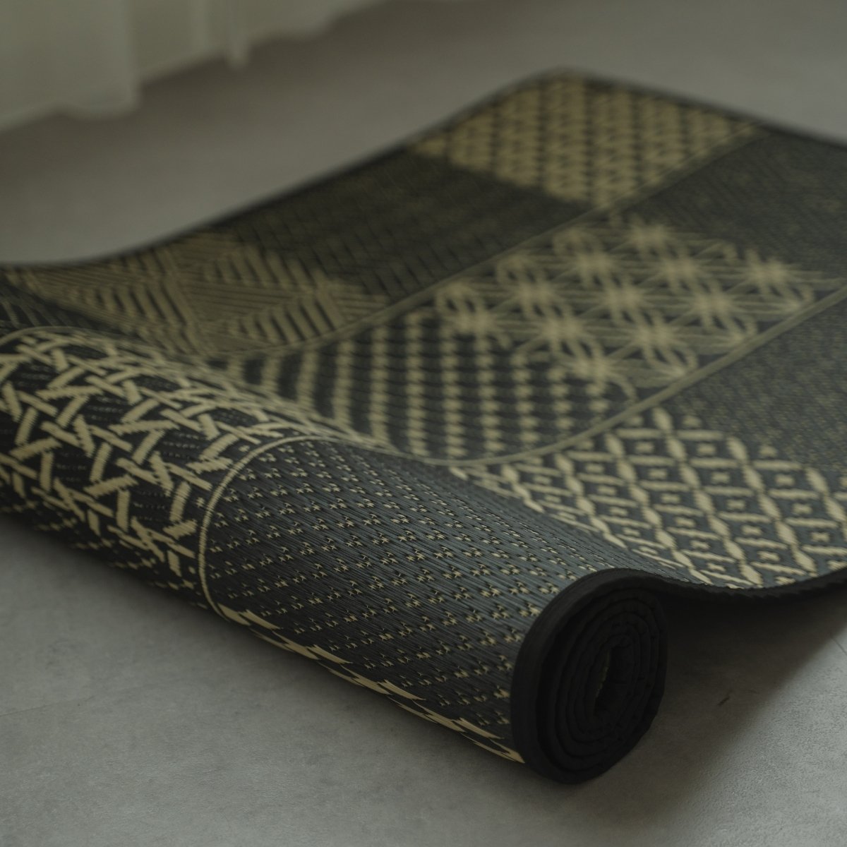 Japanse Tatami Yoga Matras "Ed Plain" Zwart gedeeltelijk opgerold, met het traditionele Edo Komon geweven patroon.