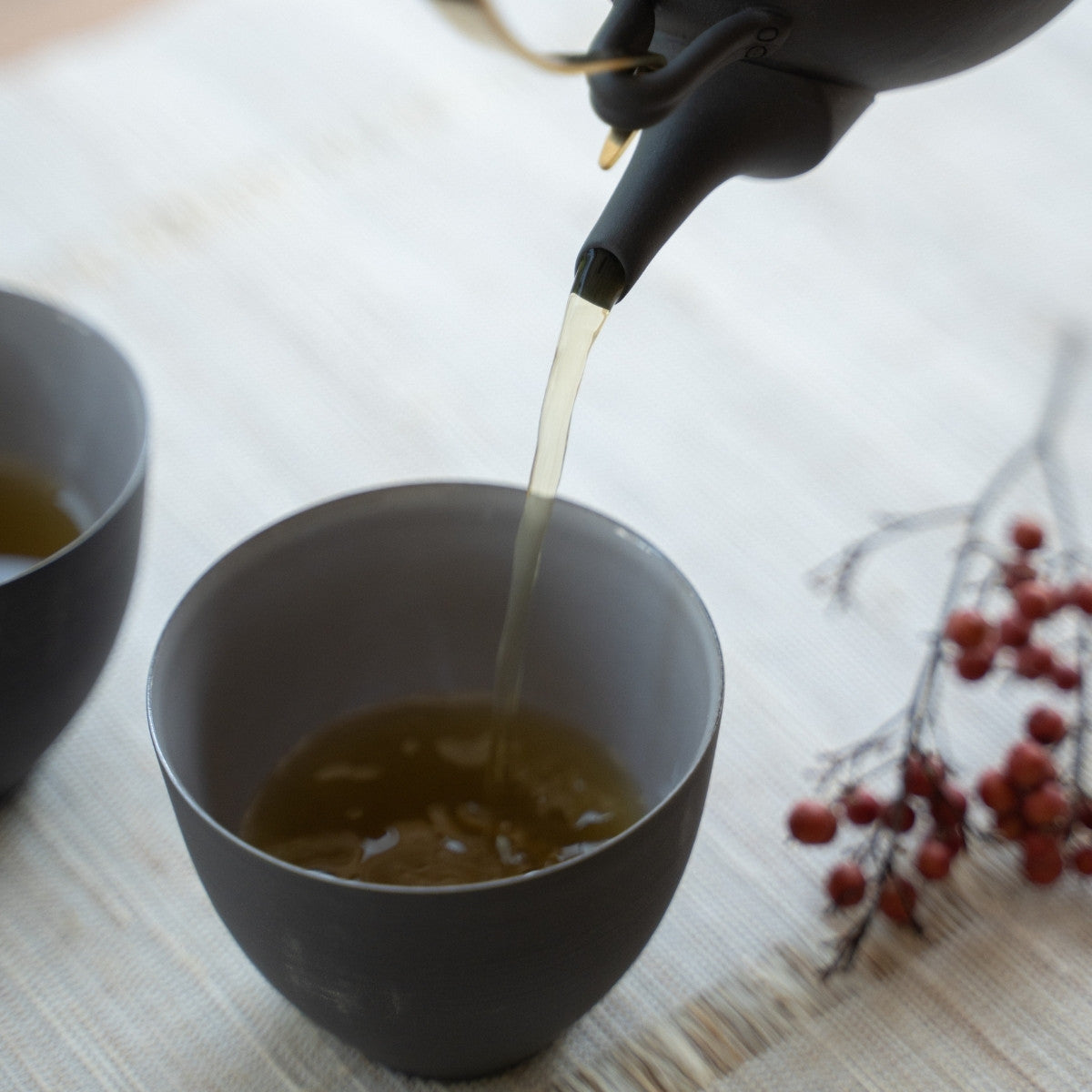 Service de thé d'une kyusu noire dans des tasses à thé japonaises dans une pièce lumineuse pour des hôtes créant une atmosphère wabi sabi.