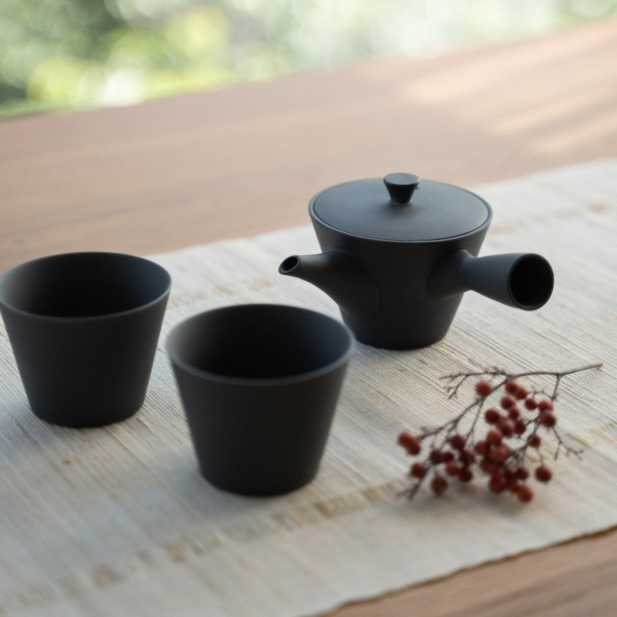Schwarze japanische Teekanne "Sencha" und Konustassen auf einem Leinenläufer für Teeliebhaber, die einen ruhigen Aufguss zubereiten.