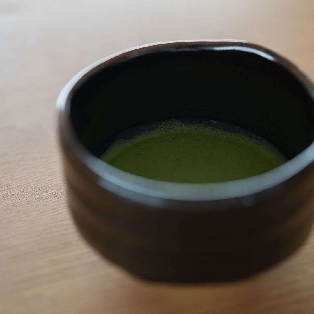 Tæt på levende smaragdgrøn matcha-te-skum inde i den dybe sorte japanske chawan-skål.