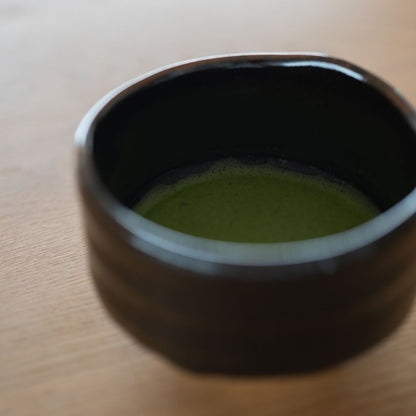 Tæt på levende smaragdgrøn matcha-te-skum inde i den dybe sorte japanske chawan-skål.