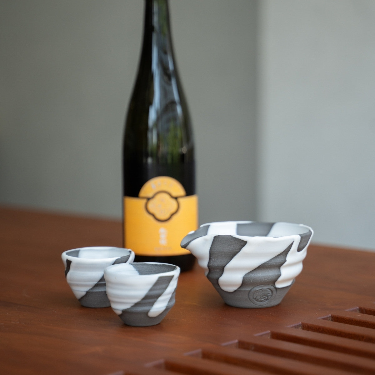 White Flow Japanese sake set, carafe and cups on a wooden table by a sake bottle, for hosting special dinners with guests