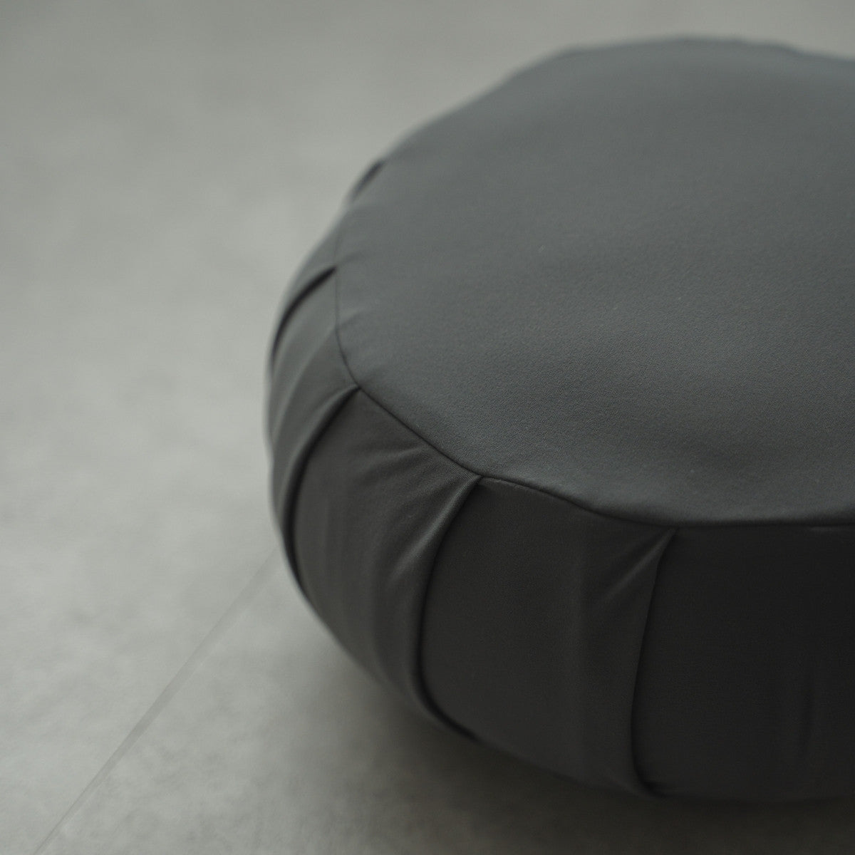 Close-up of a charcoal grey Japanese meditation cushion (zafu) showing fabric details on a modern floor for daily yoga.