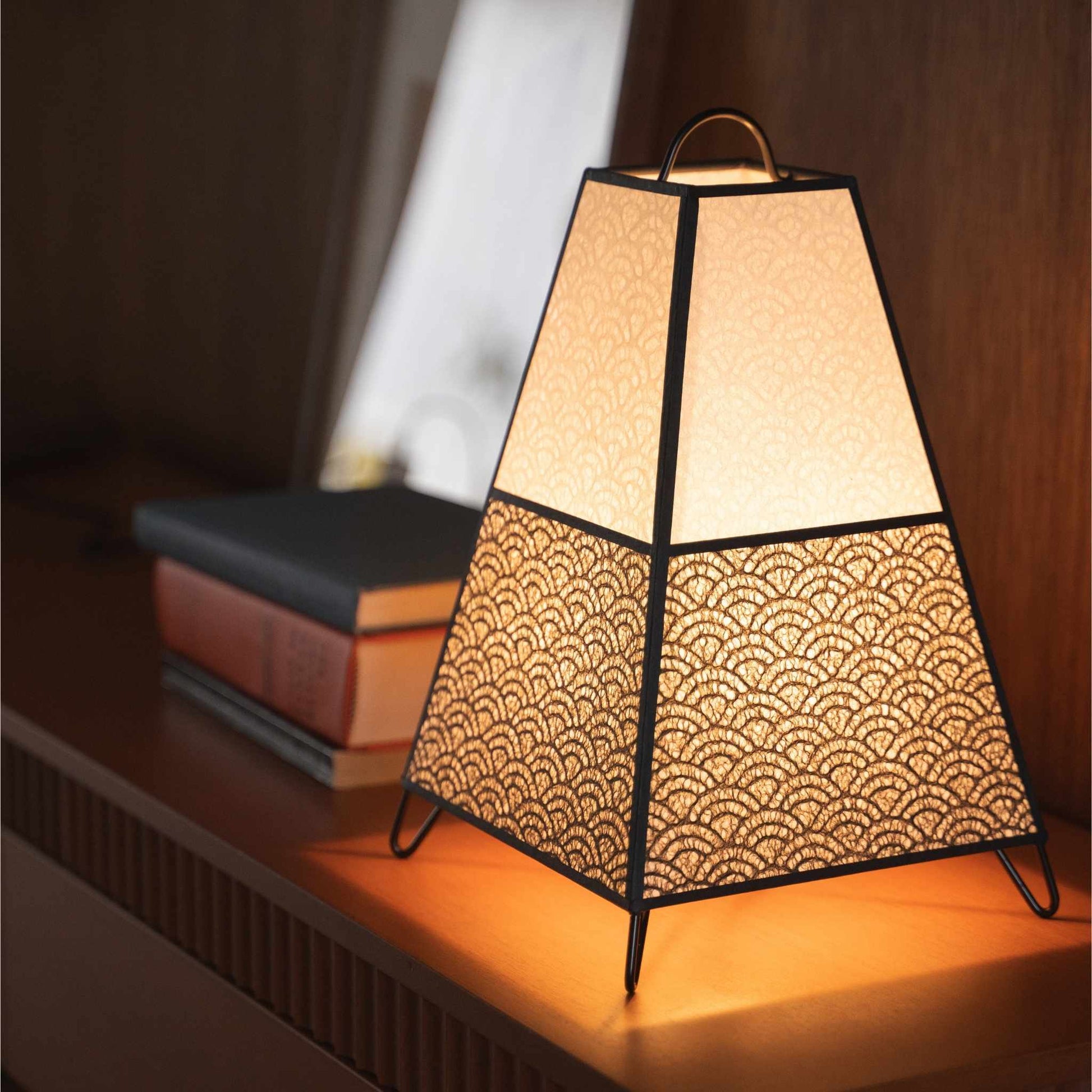 Close-up van een verlichte Japanse papieren lamp KURA Small op een console tafel, met de nadruk op het delicate Seigaiha kantpapier.