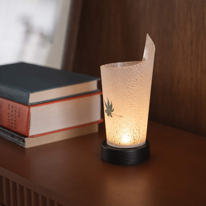 Gros plan d'une lampe de table japonaise en papier allumée "Maki" Feuille d'érable Momiji servant de lampe d'appoint chaleureuse avec une texture de papier délicate et une base en bois.