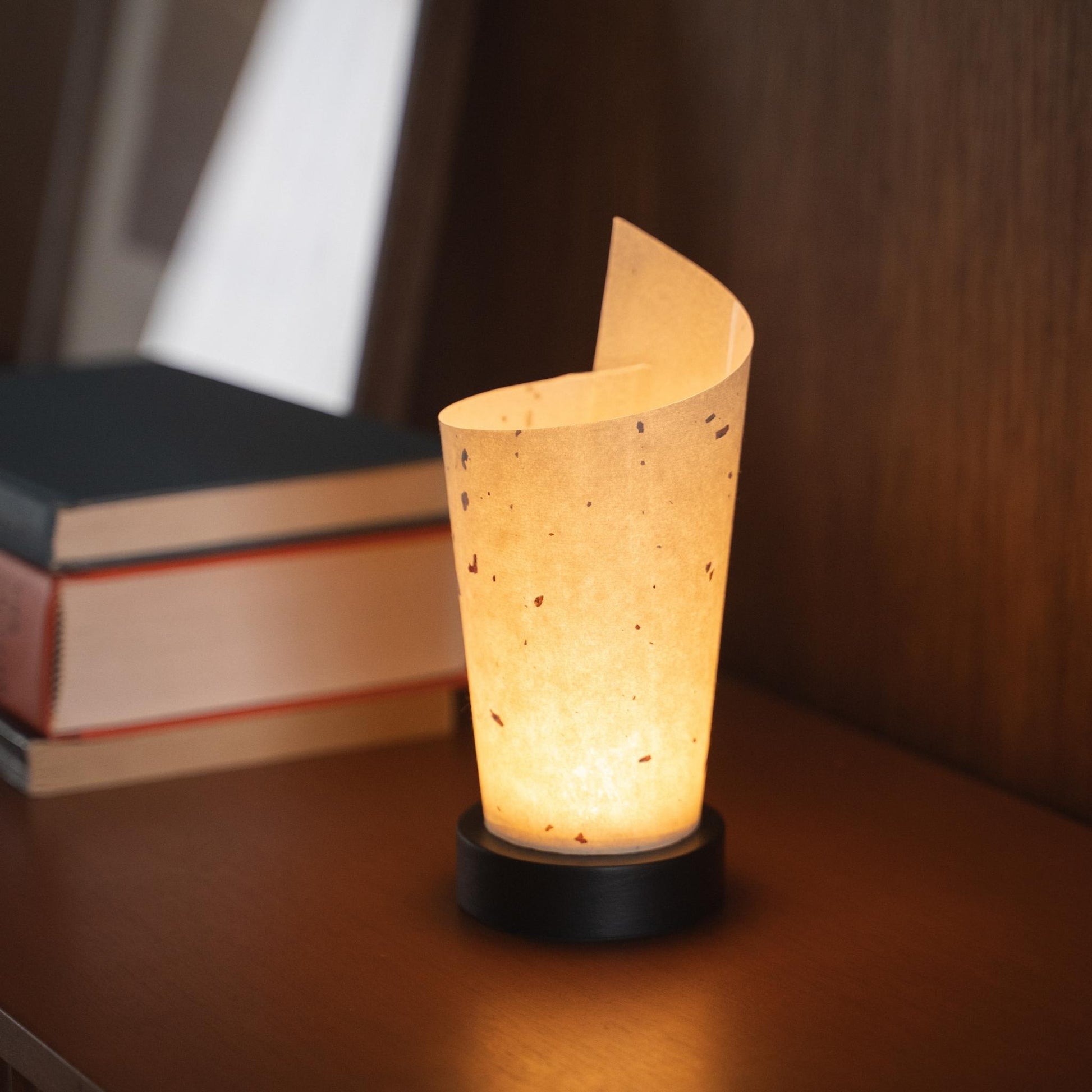 Gros plan d'une lampe de table japonaise en papier allumée "Maki" servant de lampe d'appoint chaleureuse avec une texture de papier délicate et une base en bois.
