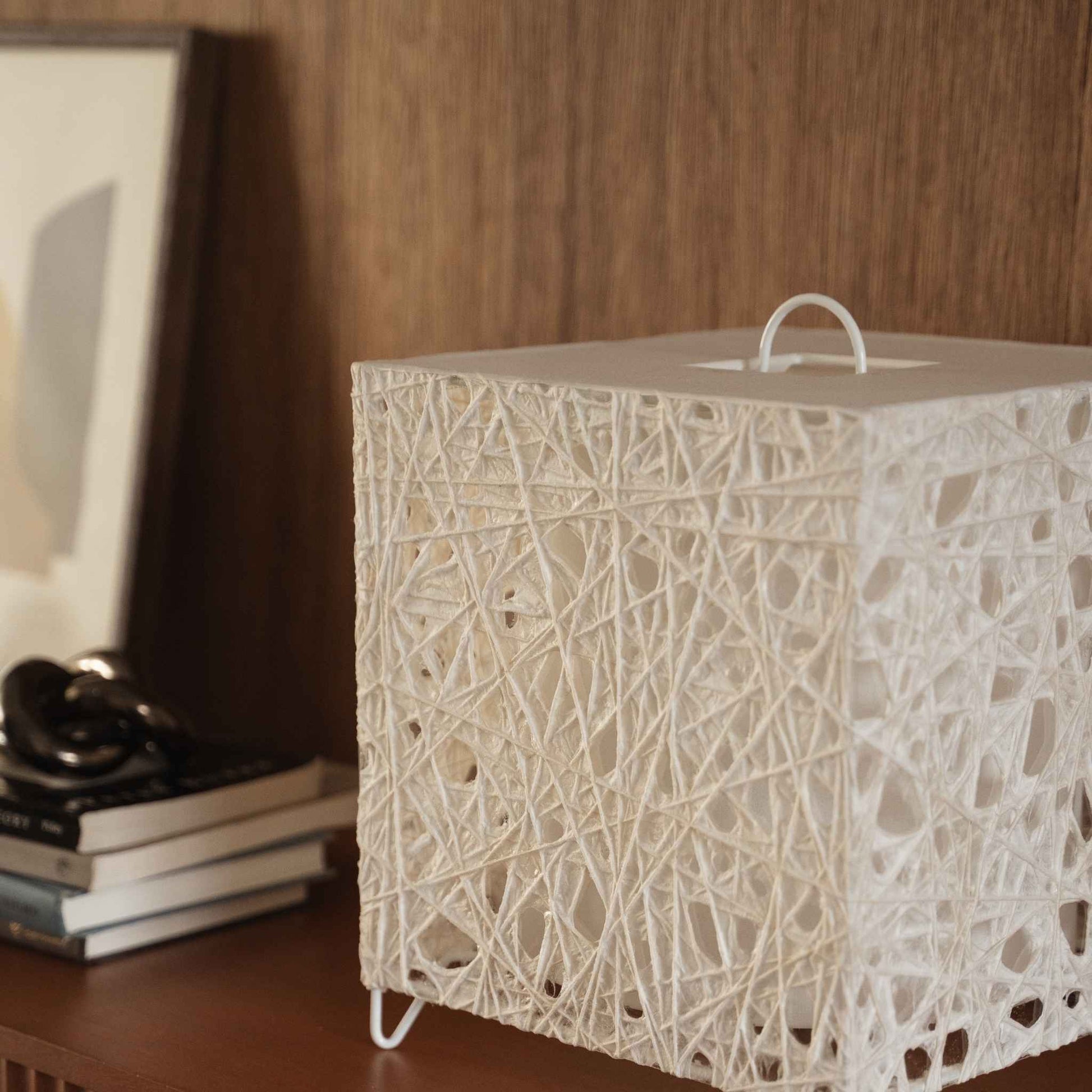 "Lampe japonaise blanche en forme de cube en papier Me Look 03, posée éteinte sur une console en bois près d'un arrière-plan de lit."
