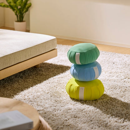 Mintegrøn, rolig blå og mimosegul japansk meditationspude zafu stablet på et tæppe til en familie zen-rutine.