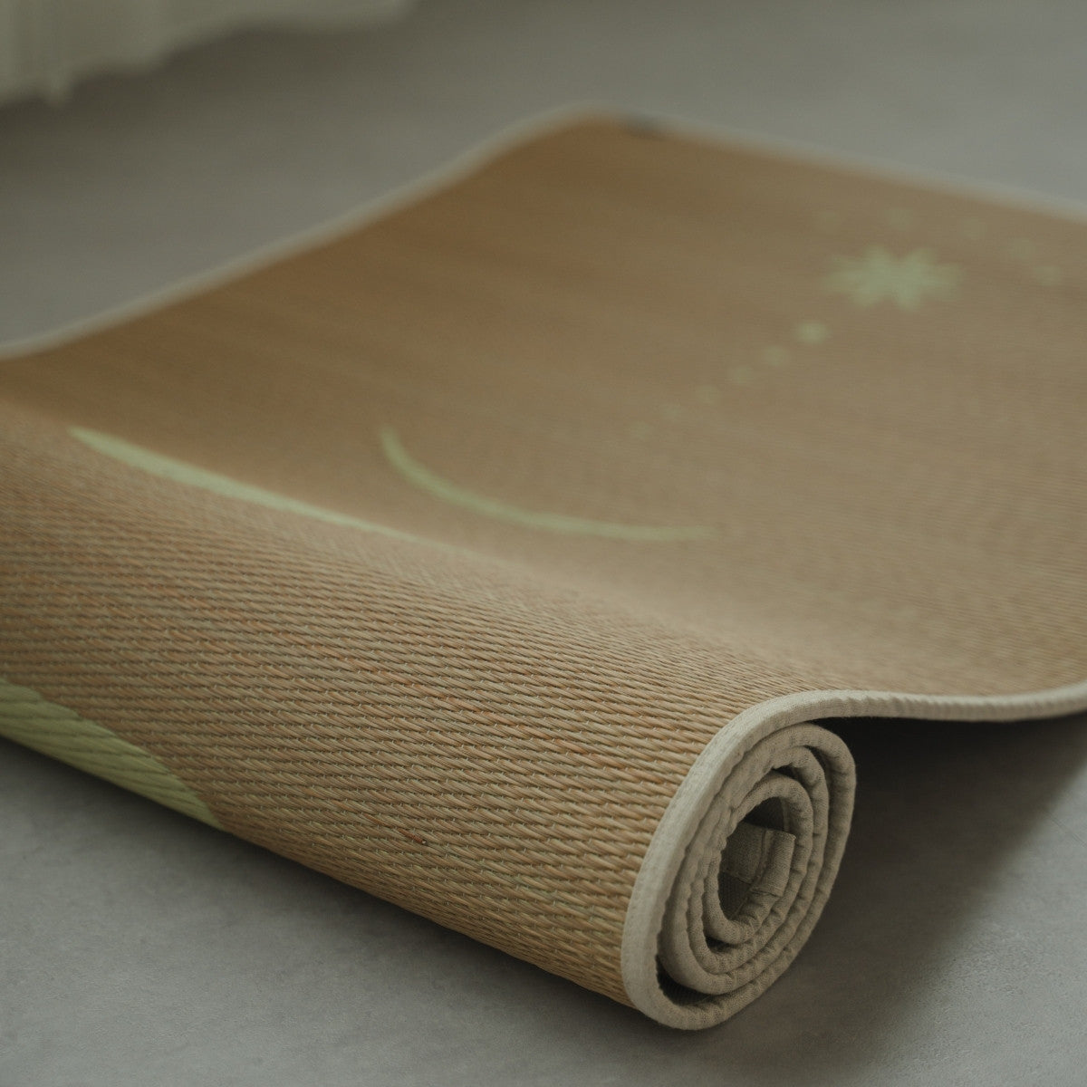 Japanse Tatami Yogamat "Maan" Beige gedeeltelijk opgerold op een grijze vloer, met zicht op de fijne textuur van natuurlijk matgras.