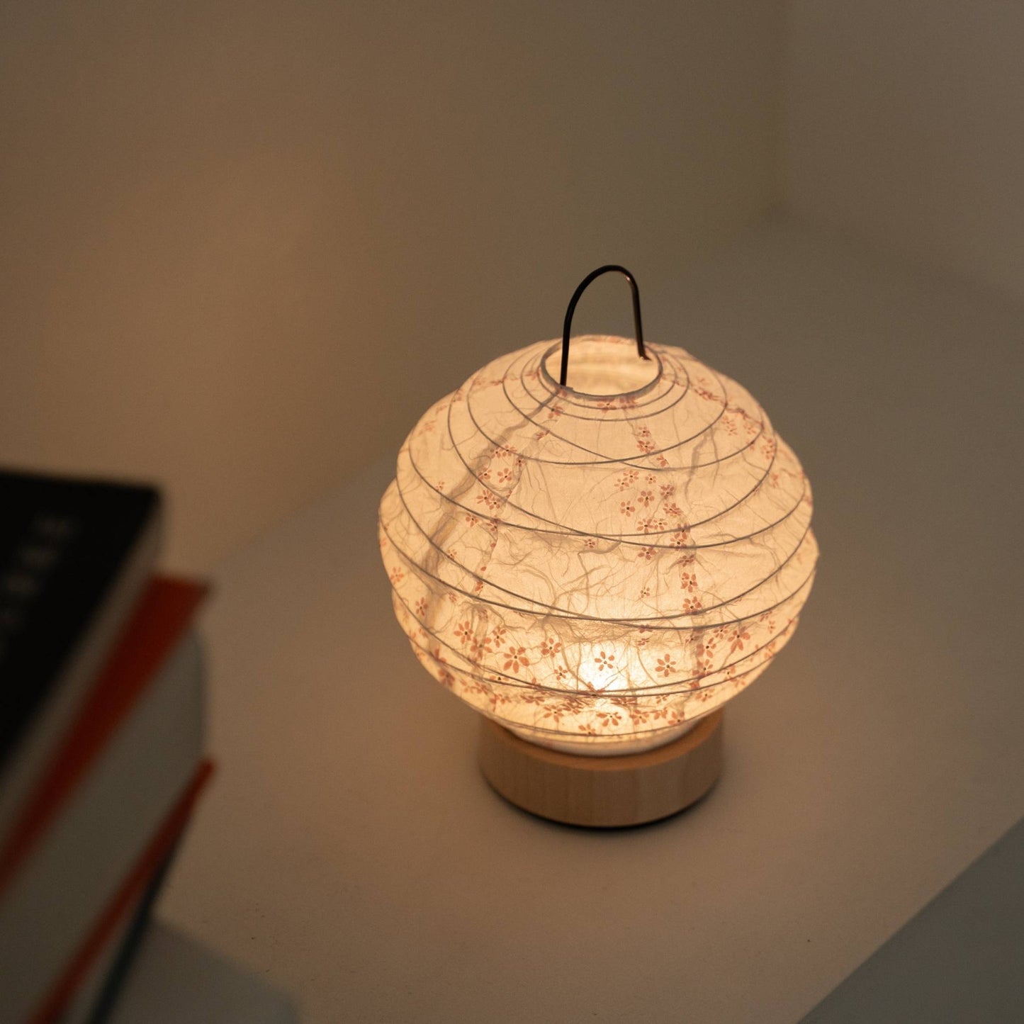Glowing round Japanese paper table lamp "Yuhi" Sakura serving as a cozy accent lamp next to books on a white console table.
