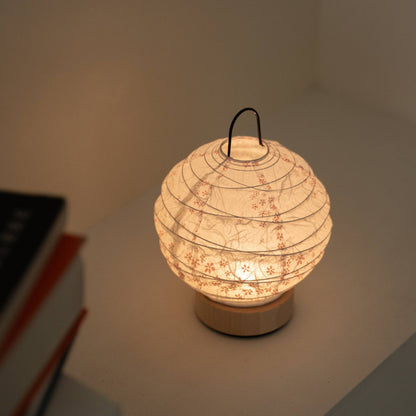Glowing round Japanese paper table lamp "Yuhi" Sakura serving as a cozy accent lamp next to books on a white console table.