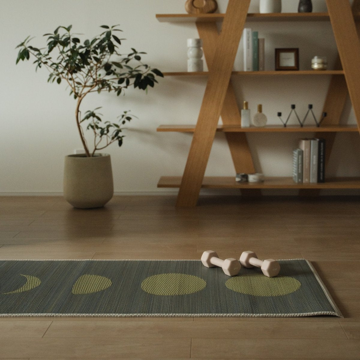 Japanse Tatami Yoga Mat "Maan" Grijs in een stijlvolle Japandi woonkamer, met kleine roze-beige dumbbells erop, voor een moderne setting voor thuisworkouts en meditatie.
